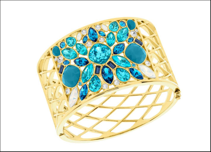 Cyan, bracciale rigido e alto in metallo Pvd oro traforato e in mezzo cristalli di tagli diversi con nuance dall'azzurro piscina a blu mare.