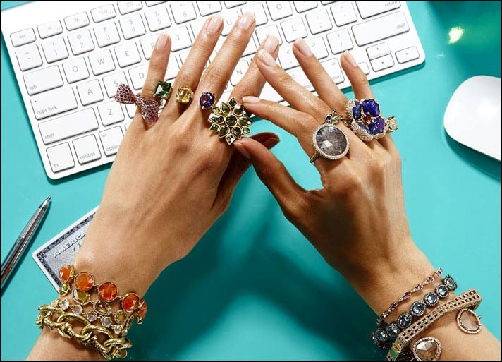 due mani femminili ricoperte di anelli di grandi dimensioni e sullo sfondo una carta di credito e una penna