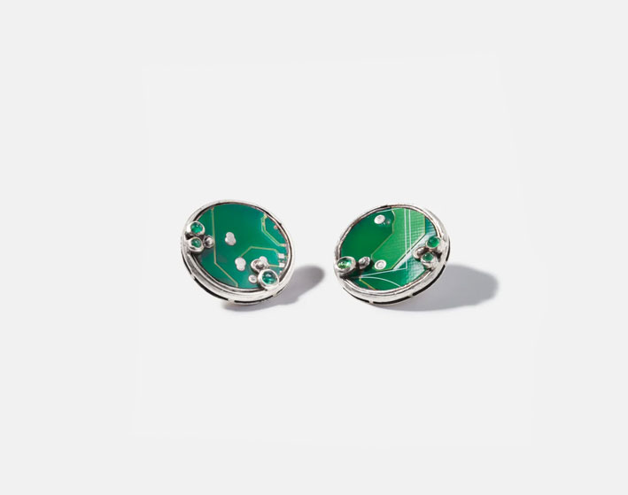 Silver Fossil Earrings feature circuit board fragments from discarded mobile phones, with responsibly sourced emeralds